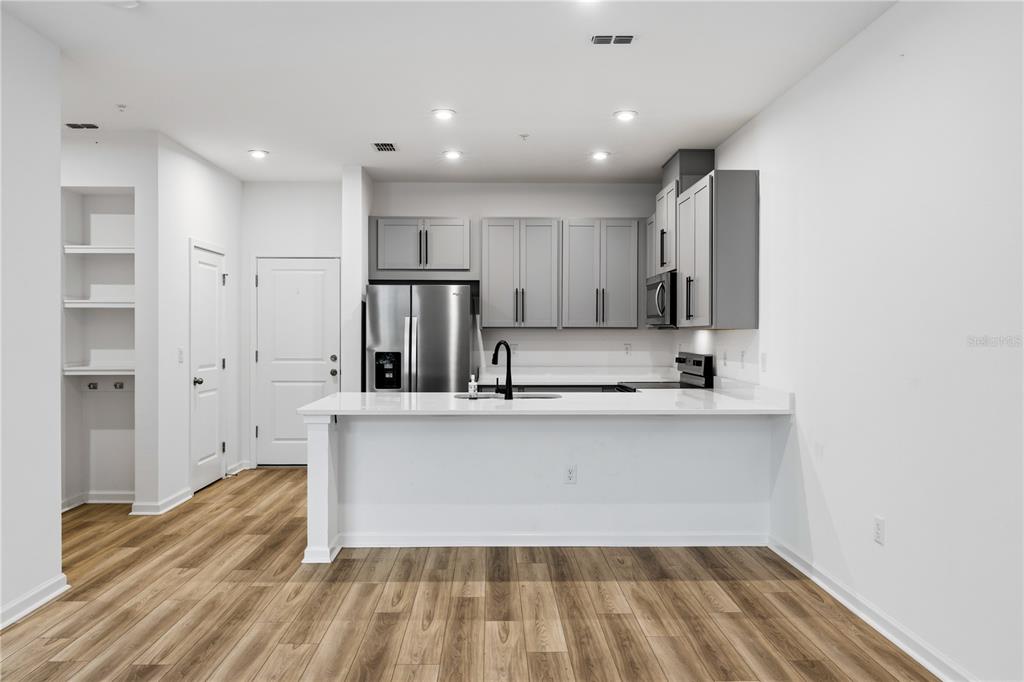 A modern kitchen features gray cabinets, stainless steel appliances, and a white quartz breakfast bar — 9844 WALKWAY DRIVE, ORLANDO, FL
