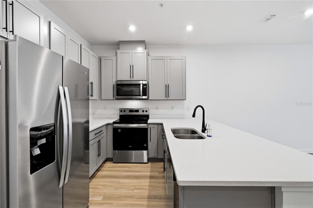 A modern kitchen features gray cabinets, stainless steel appliances, and a white quartz island countertop — 9844 WALKWAY DRIVE, ORLANDO, FL