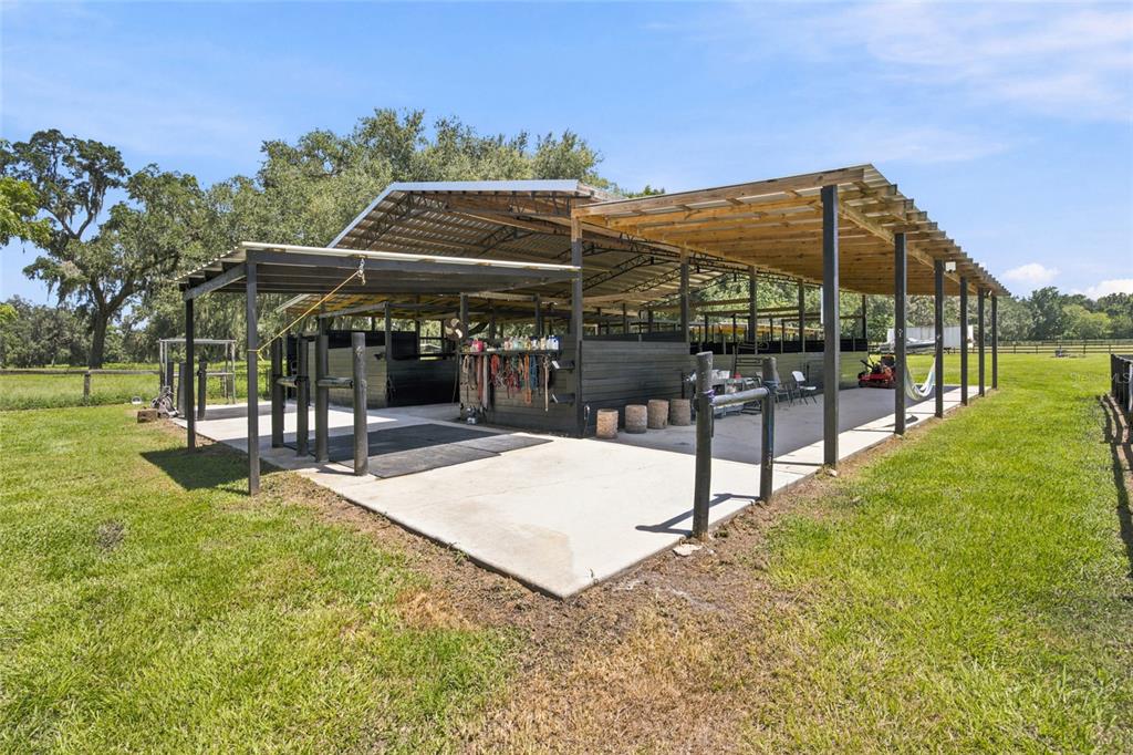 An open-air horse barn with a concrete floor and black stalls sits in a grassy field — 3875 SE 118TH LANE, BELLEVIEW, FL
