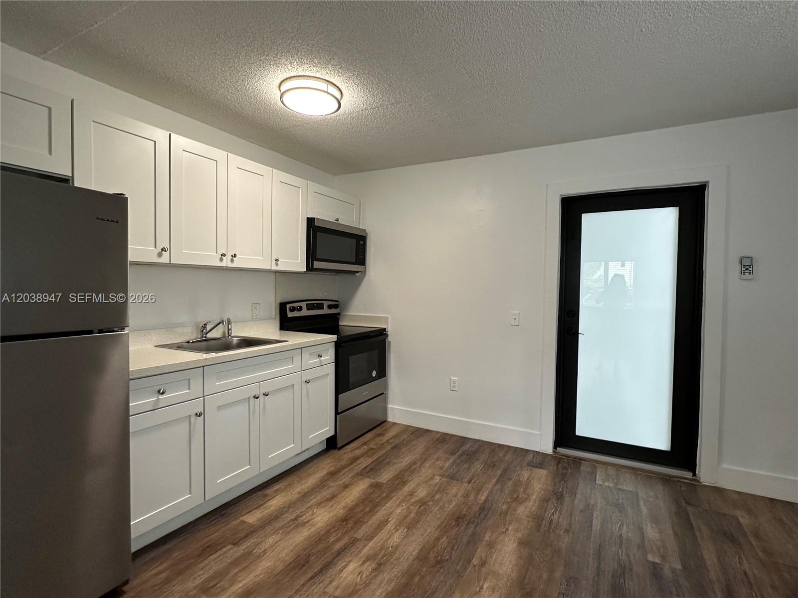 A kitchen features white cabinets, stainless steel appliances, and wood-look flooring near a glass door — 529 SW 4th St # 104, Miami FL 33130, MIAMI, FL