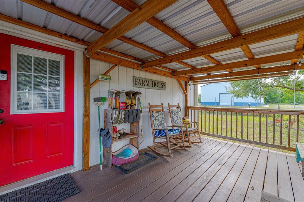 A covered wooden porch features a red door, rocking chairs, and a shoe rack — 4536 EMPIRE CHURCH RD, GROVELAND, FL