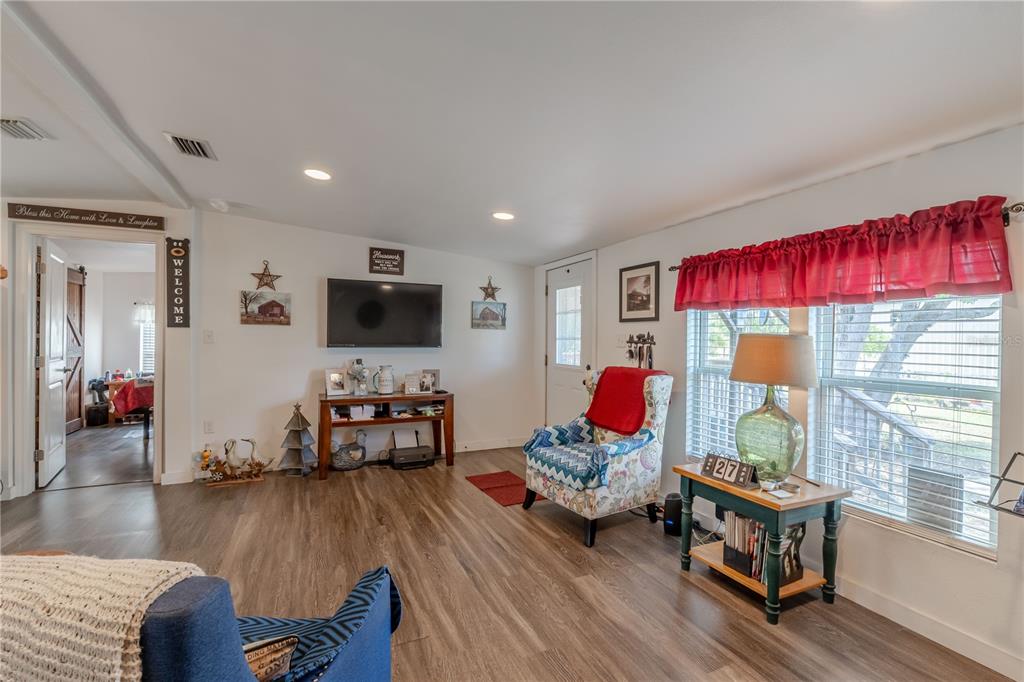 A living room features wood-look flooring, a wall-mounted television, a patterned armchair, and a window — 4536 EMPIRE CHURCH RD, GROVELAND, FL