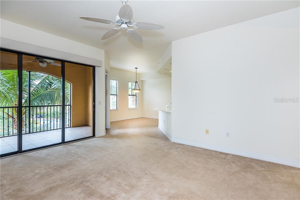 A carpeted living room features a ceiling fan, sliding glass doors, and an adjacent dining area — 97 VIVANTE BOULEVARD UNIT 304, PUNTA GORDA, FL