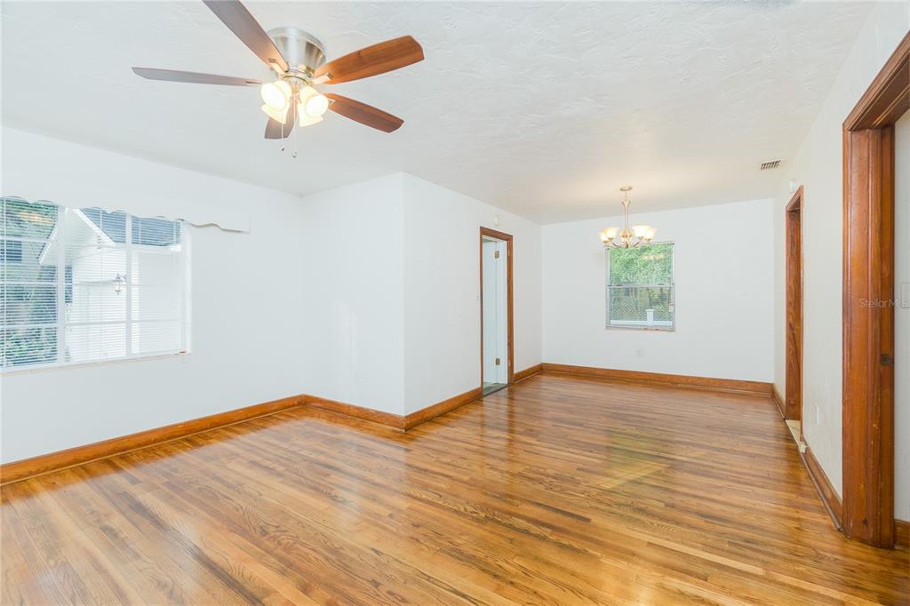 An empty room with hardwood floors, white walls, a ceiling fan, and a chandelier — 920 NW 20TH STREET, GAINESVILLE, FL