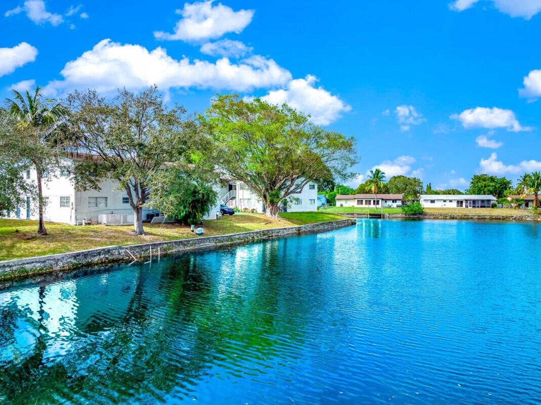 A view of a waterfront apartment building with large trees and a blue sky — COCONUT CREEK, FL