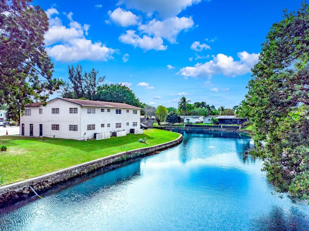 An aerial view of a two-story white apartment building situated beside a blue canal — COCONUT CREEK, FL