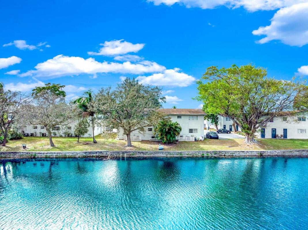 A multi-story apartment building sits along a waterfront with trees and a blue sky — COCONUT CREEK, FL