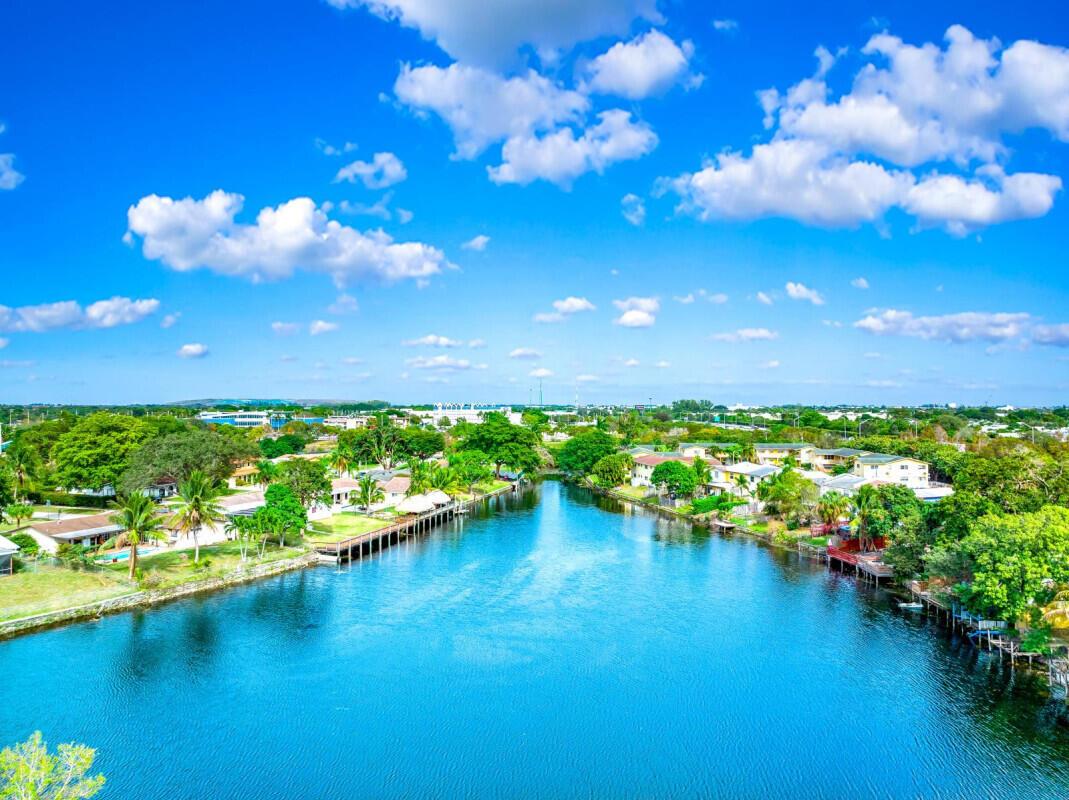 An aerial view of a canal flowing between residential properties surrounded by lush green trees — COCONUT CREEK, FL