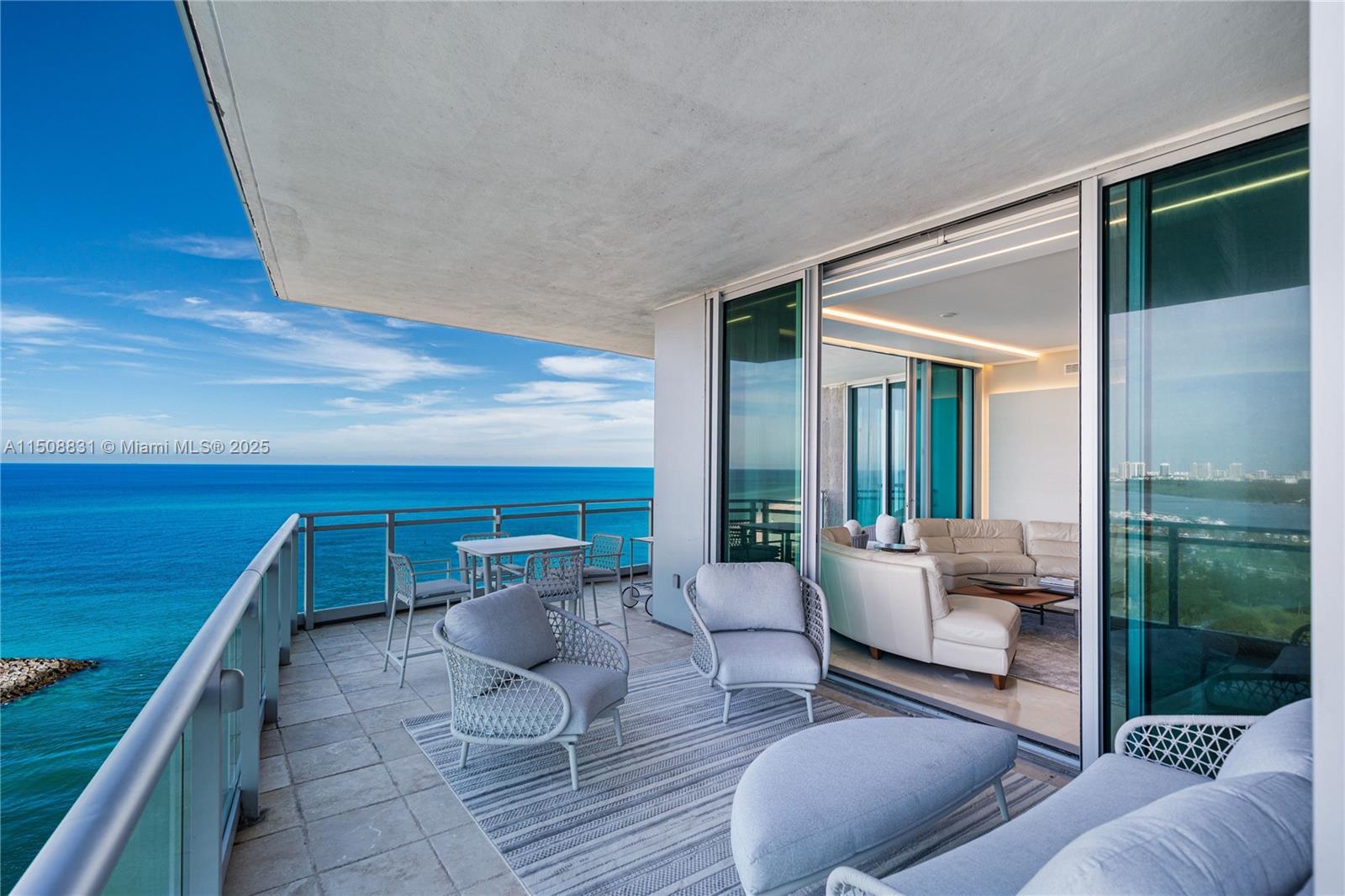 A balcony with outdoor seating overlooks the ocean next to a modern living room — 10295 E Collins Ave # 1509, Bal Harbour FL 33154, BAL HARBOUR, FL