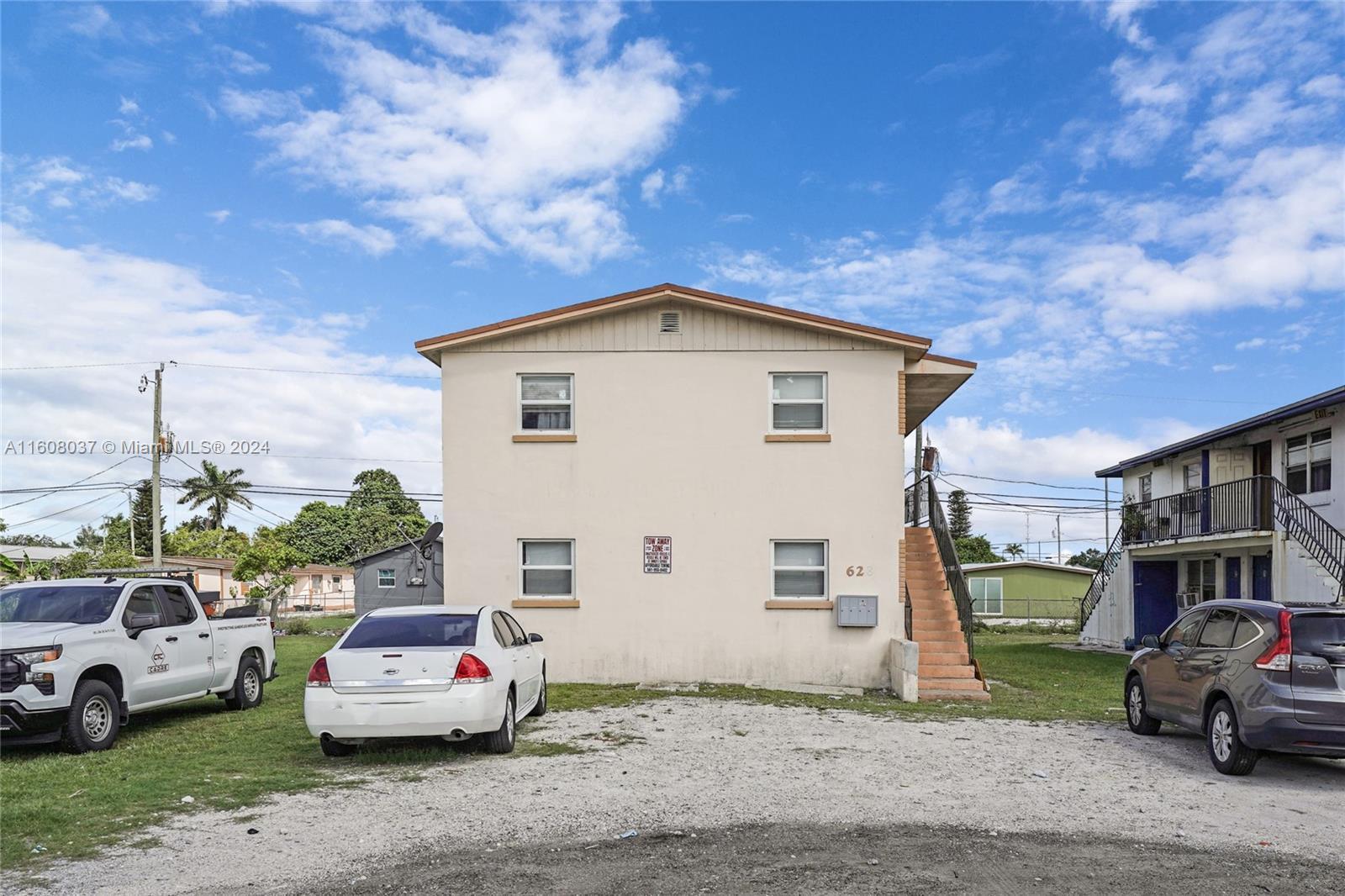 A two-story beige apartment building features an exterior staircase and a gravel parking lot — 628 SW 4th Street, Belle Glade FL 33430, BELLE GLADE, FL