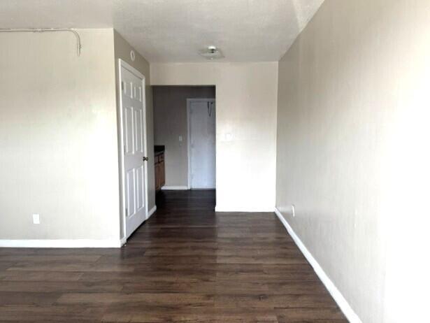A room with light-colored walls and dark wood-look flooring leads to a doorway — 628 SW 4th Street, Belle Glade FL 33430, BELLE GLADE, FL