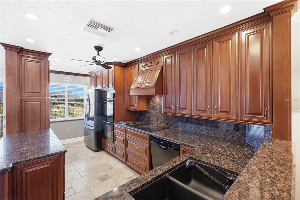 A kitchen features dark wood cabinets, granite countertops, stainless steel appliances, and tile flooring — 1600 1ST AVENUE W UNIT 506, BRADENTON, FL