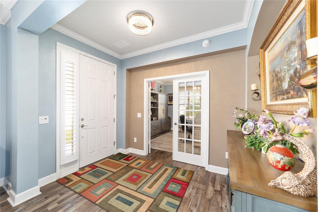 An entryway with wood-look flooring, a colorful area rug, and French doors leading to an office — 6612 SW 91ST CIRCLE, OCALA, FL