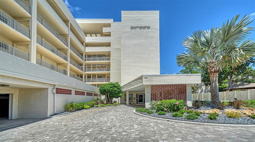 A multi-story apartment building features a paved driveway, a covered entrance, and a palm tree — 1355 S PORTOFINO DRIVE UNIT 103, SARASOTA, FL
