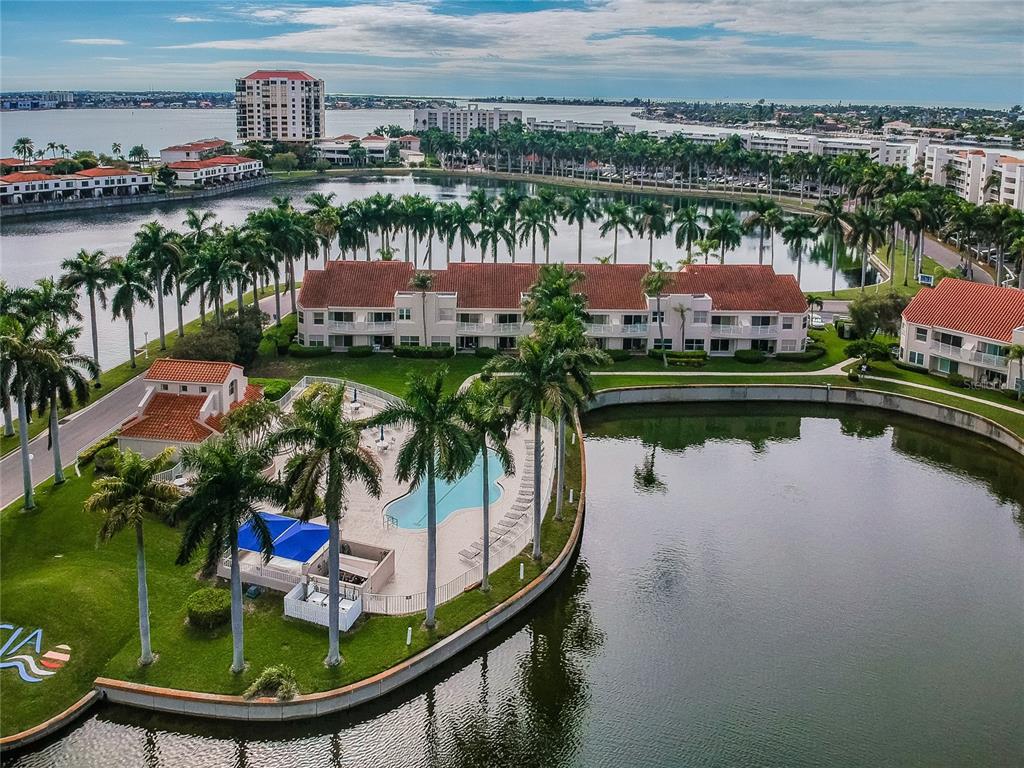 An aerial view shows a swimming pool, palm trees, and multi-story buildings beside a lake — 6073 BAHIA DEL MAR BOULEVARD UNIT 129, ST PETERSBURG, FL