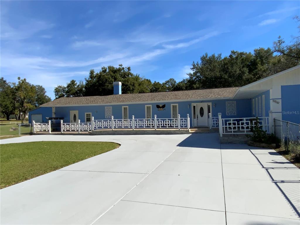 A blue single-story house features a white fence, a large concrete driveway, and a chimney — 39742 GELLA WAY, LADY LAKE, FL