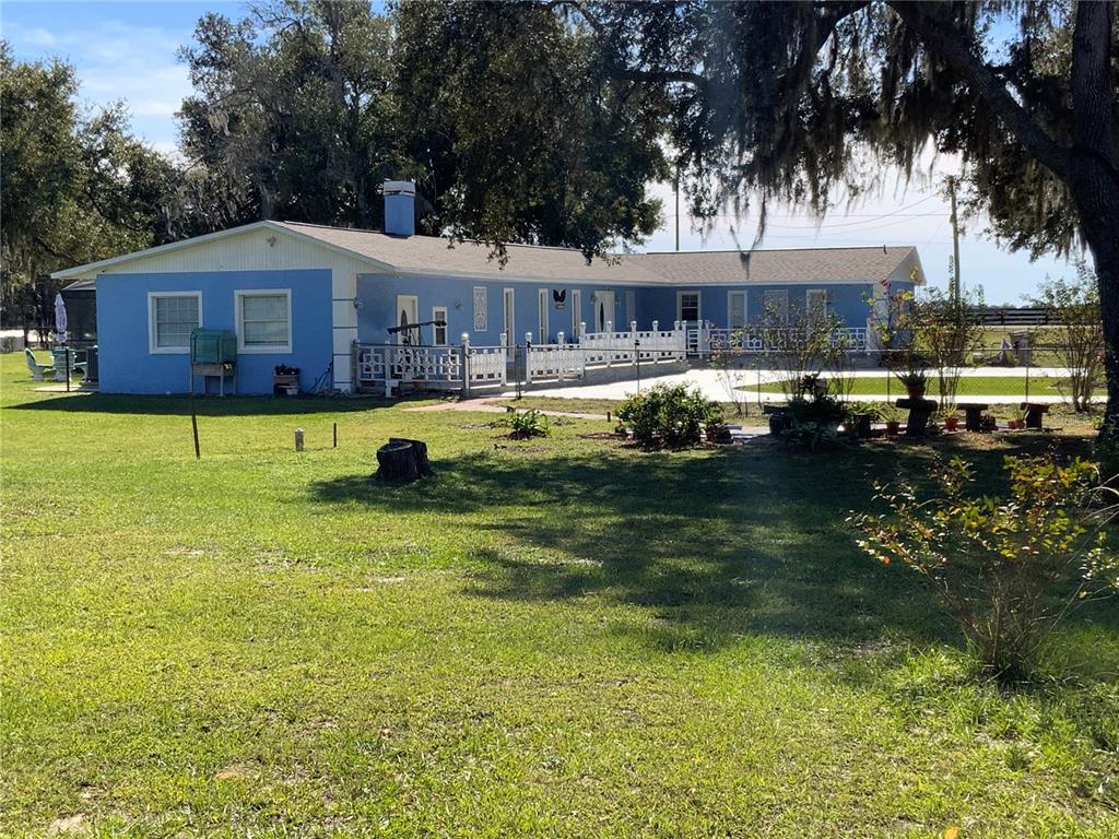 A blue, single-story ranch-style house features a white porch railing and a large grassy yard — 39742 GELLA WAY, LADY LAKE, FL