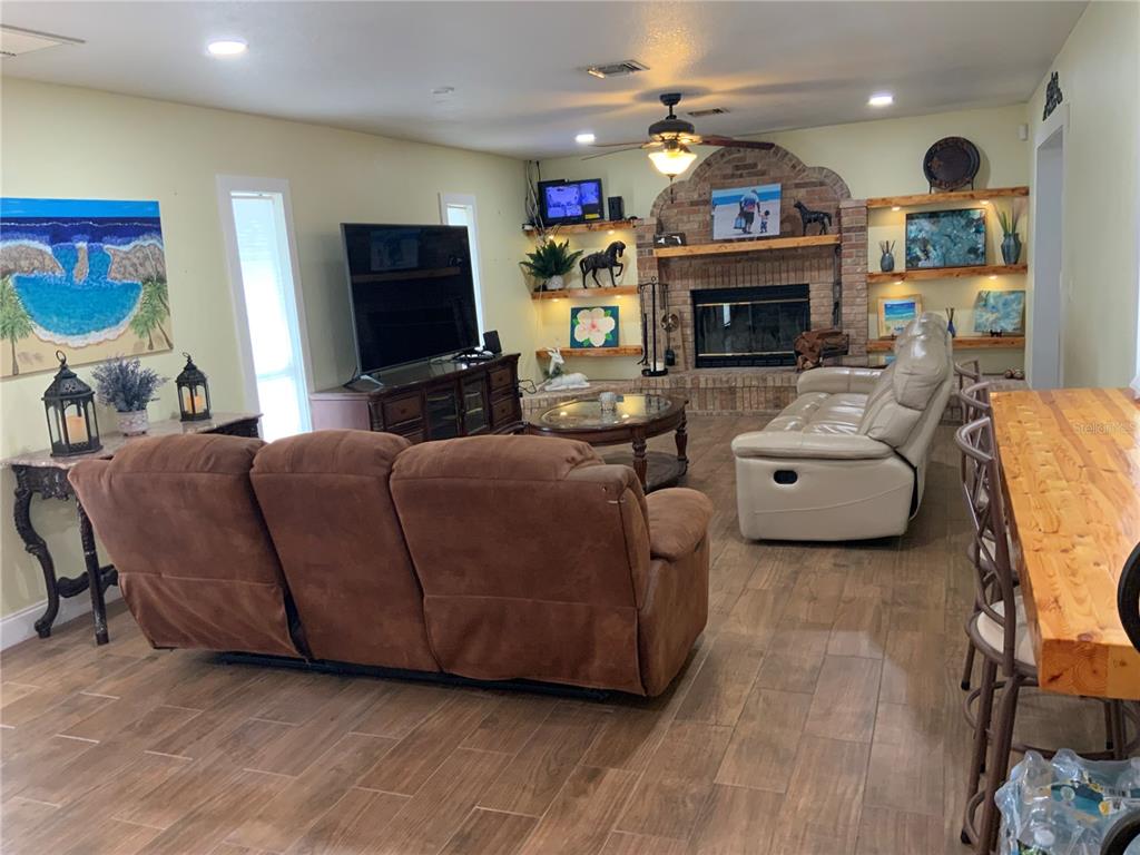 A living room features a brick fireplace, brown reclining sofa, beige leather sofa, and wood-look flooring — 39742 GELLA WAY, LADY LAKE, FL