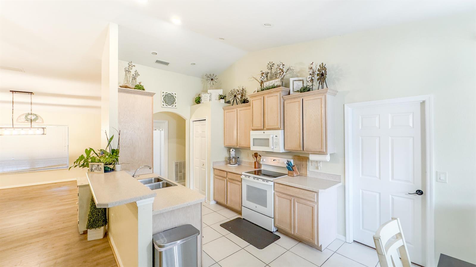 A kitchen features light wood cabinets, white appliances, a peninsula, and tile flooring — 9134 Oviedo Street, Sebring FL 33872, SEBRING, FL