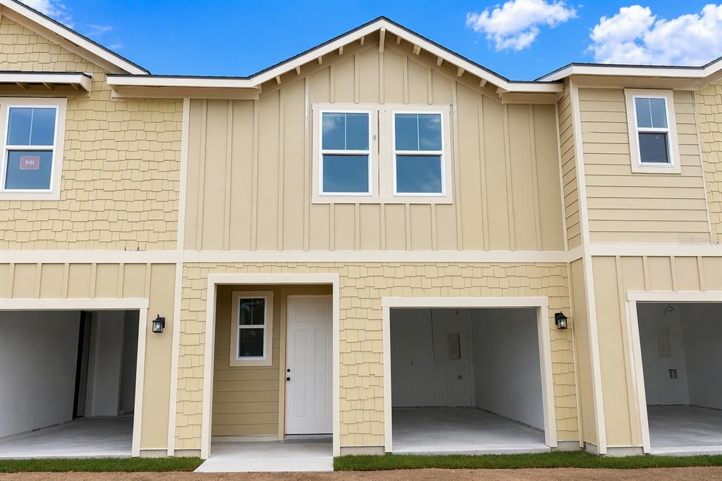 A two-story townhouse exterior features tan siding, a white front door, and two open garages — 7540 DEER VALLEY CIRCLE, TAMPA, FL