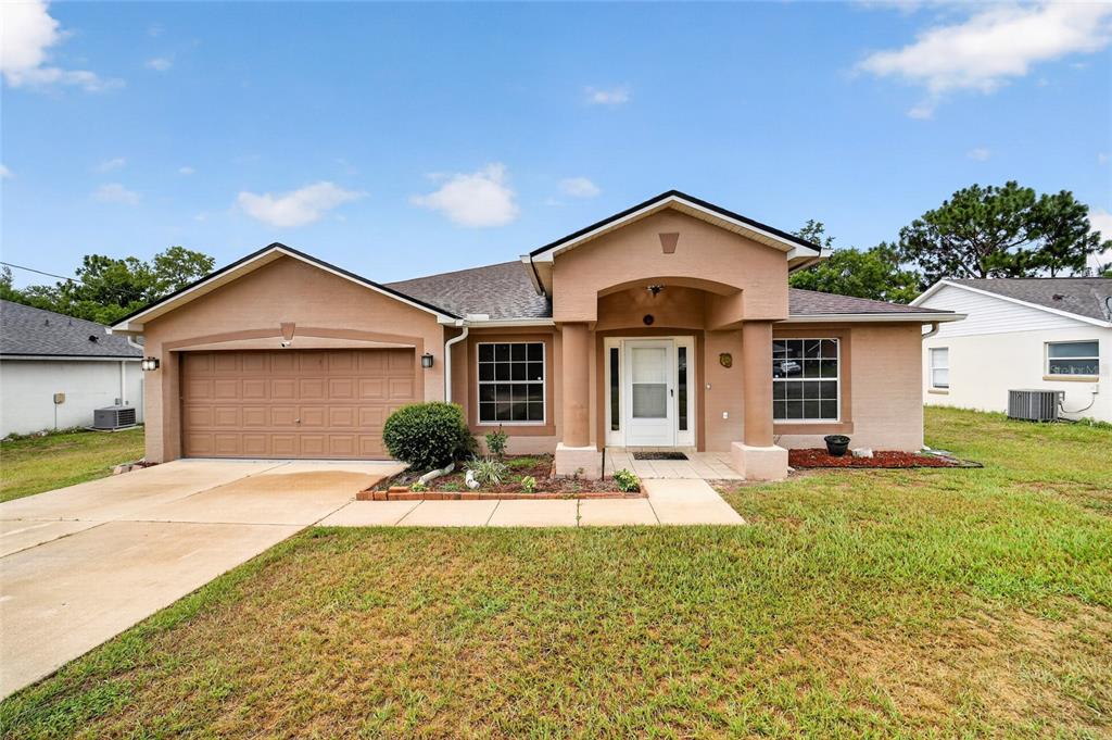 A single-story tan stucco house with a two-car garage and a covered front entryway — 5115 PECAN ROAD, OCALA, FL