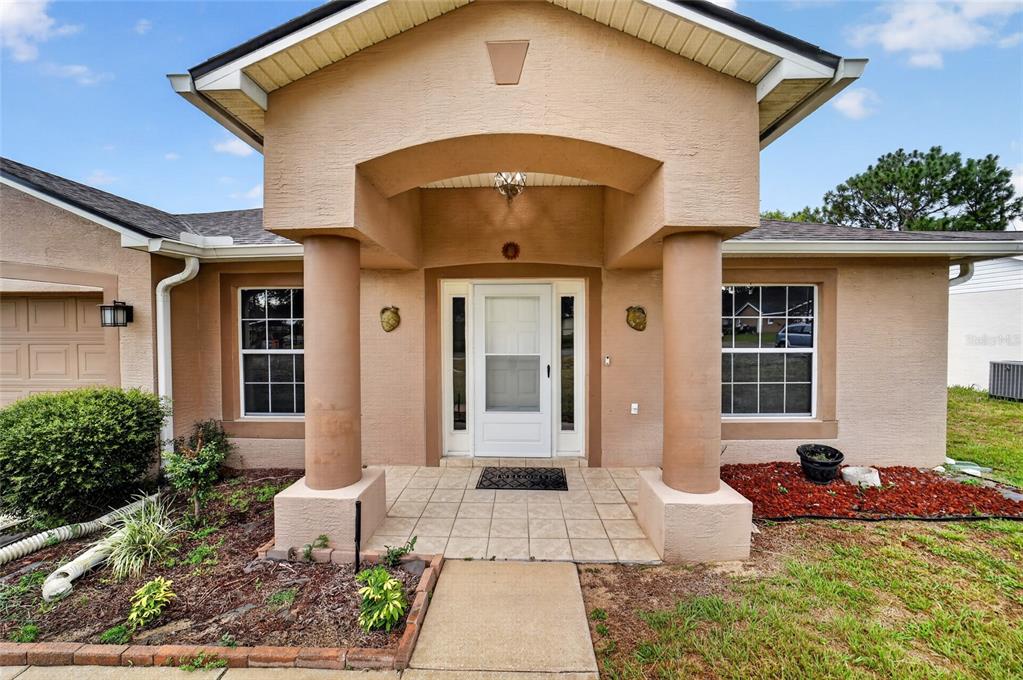 The exterior of a tan stucco house features a covered entryway with two large columns — 5115 PECAN ROAD, OCALA, FL