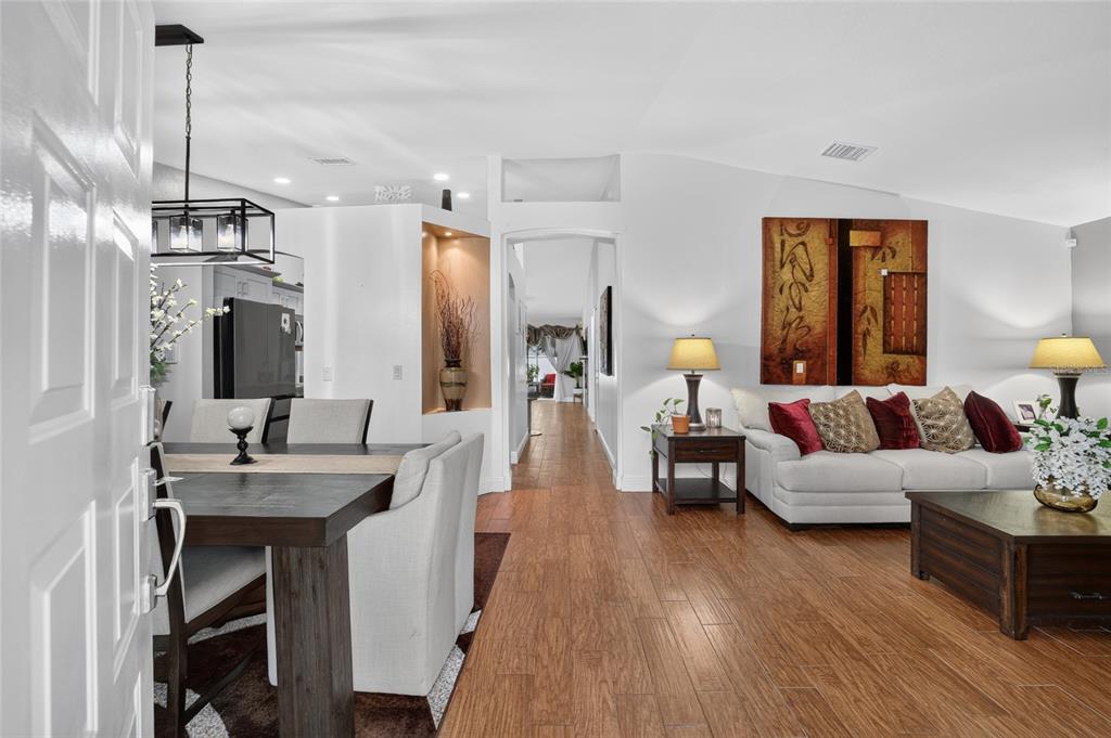 An open-concept living and dining area features wood-look tile flooring and a neutral color palette — 5115 PECAN ROAD, OCALA, FL