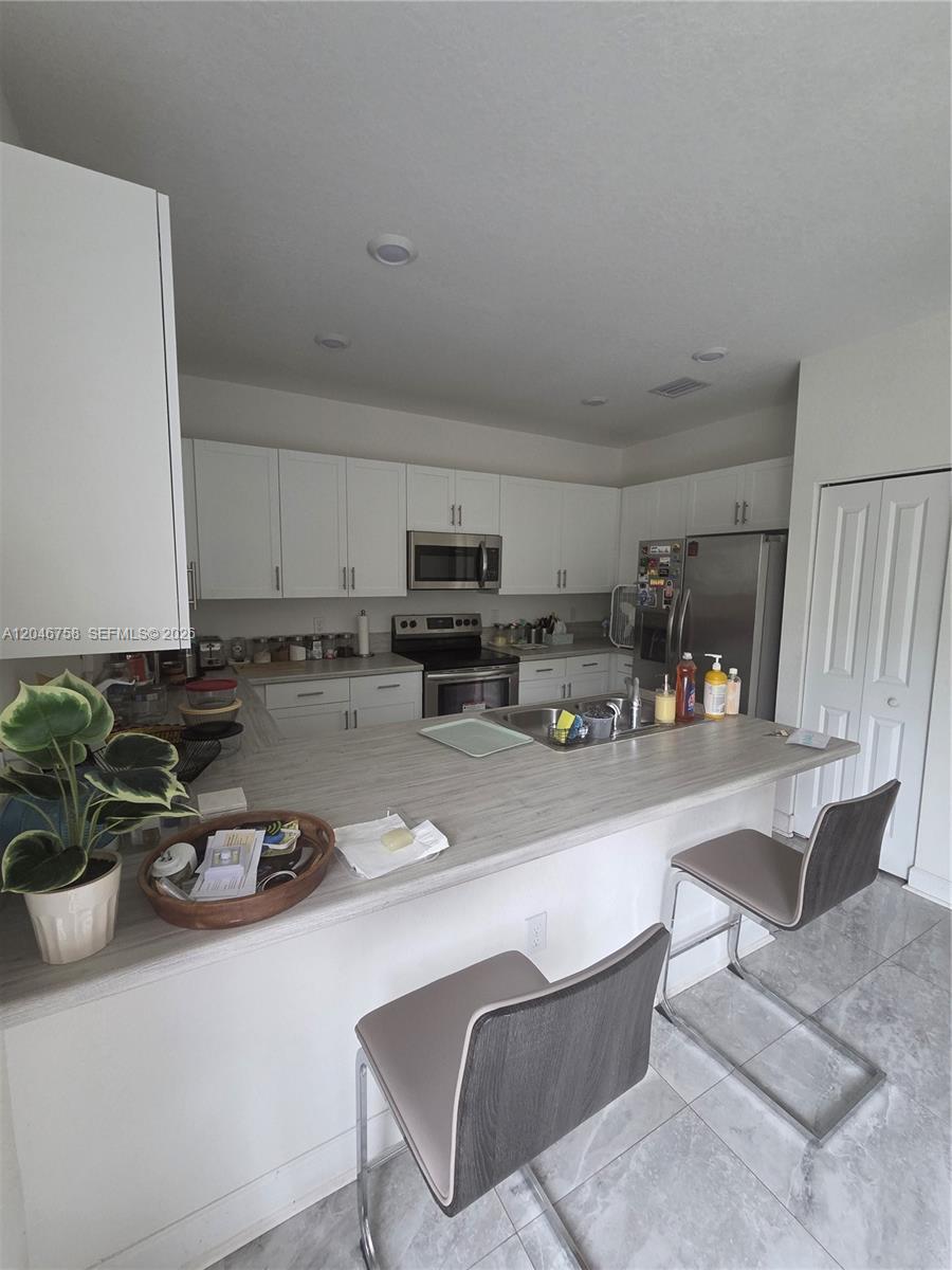 A kitchen features white cabinetry, stainless steel appliances, and a light wood-look breakfast bar — 21124 NE 8th Ave # 211, Miami FL 33179, MIAMI, FL