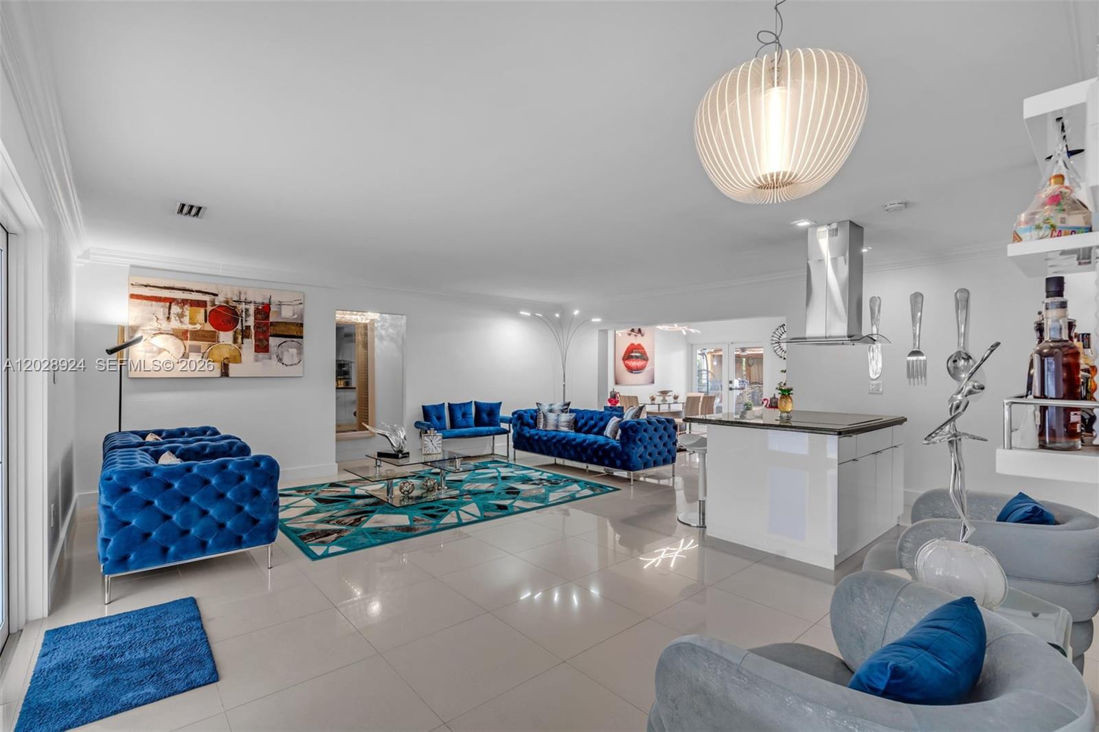 A bright, open-concept living room features blue tufted sofas, a geometric rug, and a kitchen island — 46 NE 164th St # 0, Miami FL 33162, MIAMI, FL