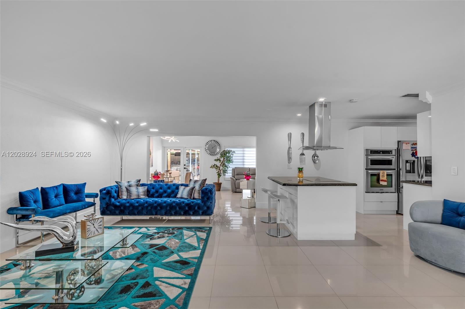 A living room and kitchen area feature blue tufted furniture, tile floors, and white cabinetry — 46 NE 164th St # 0, Miami FL 33162, MIAMI, FL