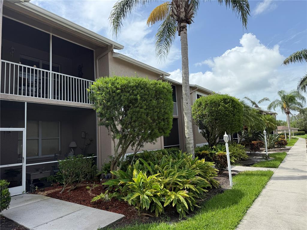 A two-story apartment building features screened-in balconies, manicured landscaping, and a sidewalk along the exterior — 5320 HYLAND HILLS AVENUE UNIT 2222, SARASOTA, FL