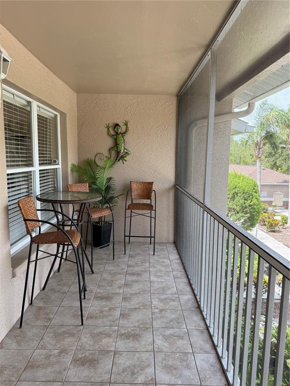 A screened-in balcony features tiled flooring, a high-top table with two chairs, and a wall-mounted lizard — 5320 HYLAND HILLS AVENUE UNIT 2222, SARASOTA, FL