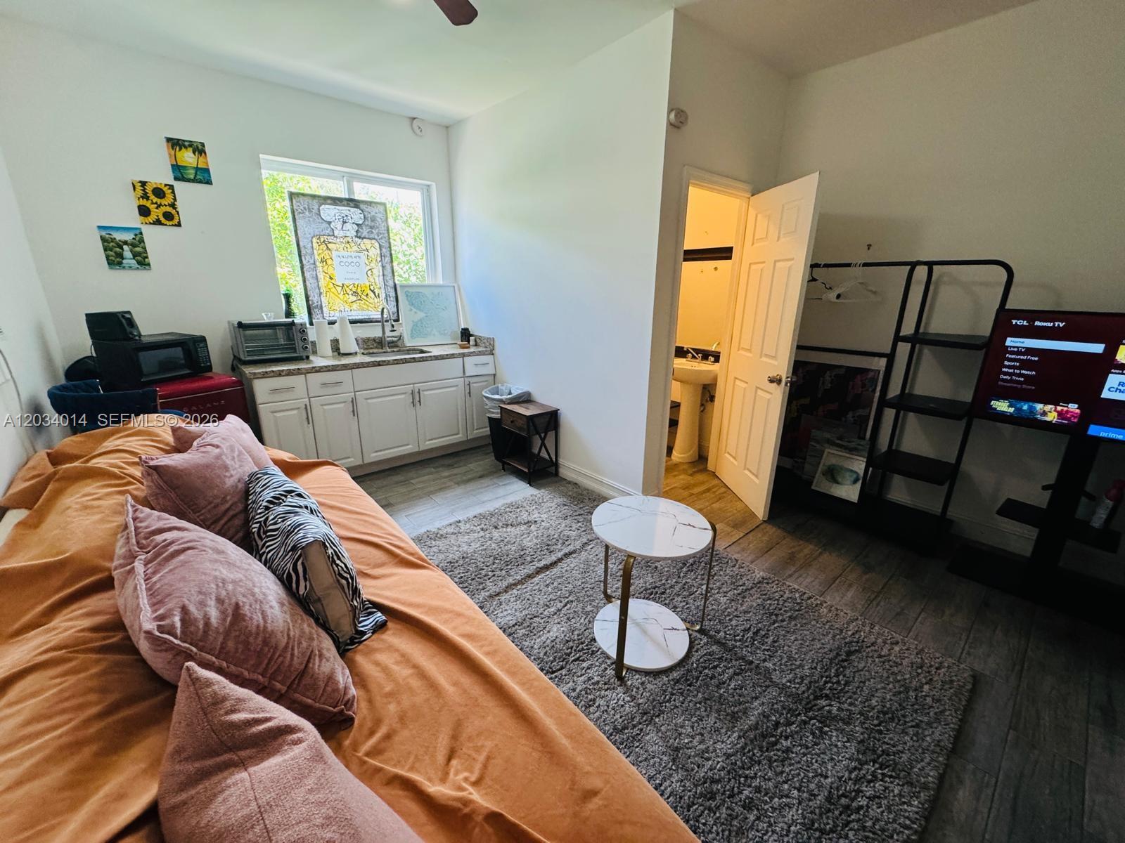 A studio apartment features a kitchenette, a bed with orange bedding, and an attached bathroom — 11 NW 47th Ter # 1B, Miami FL 33127, MIAMI, FL