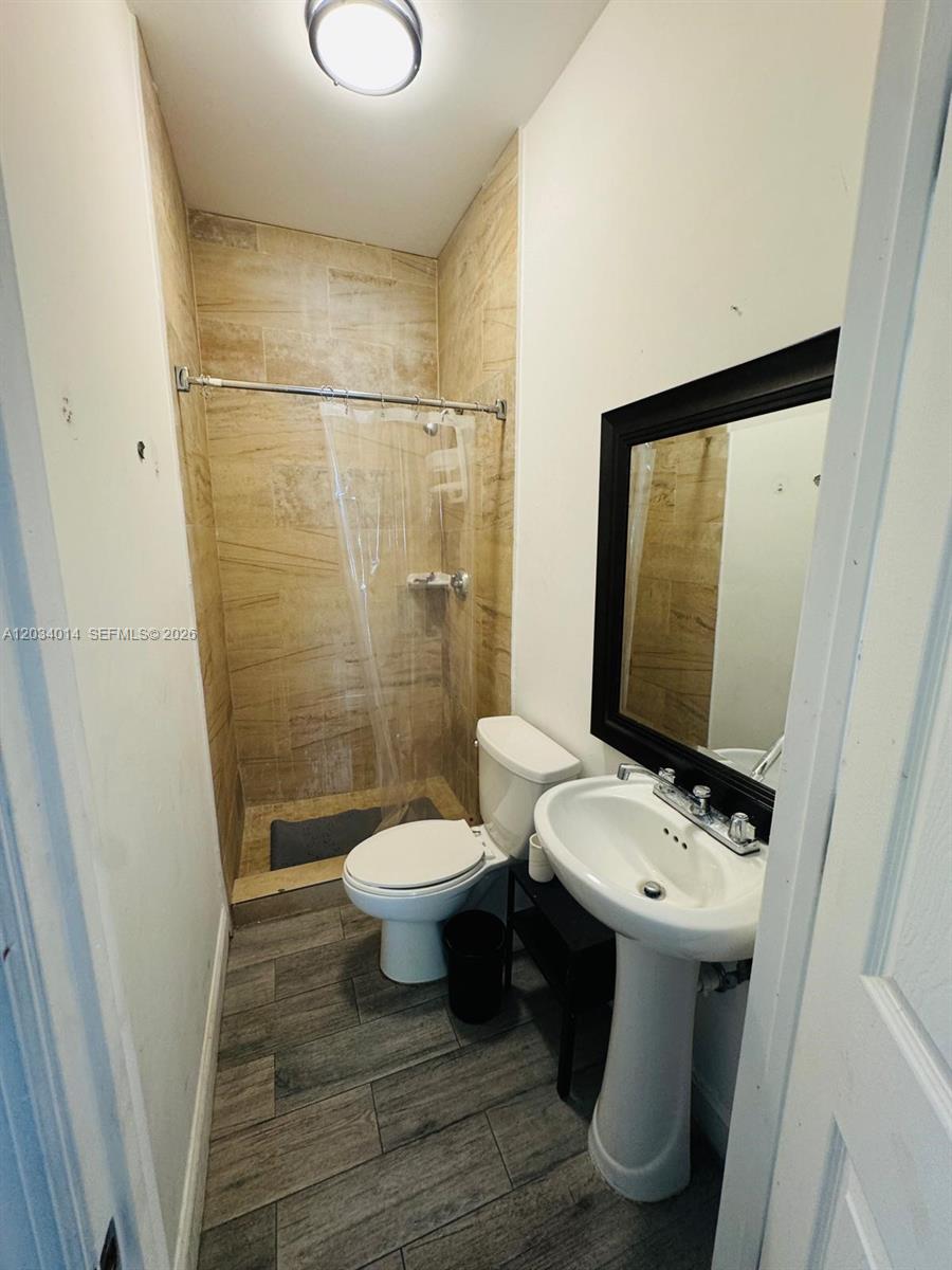A small bathroom features a pedestal sink, a toilet, and a tiled walk-in shower — 11 NW 47th Ter # 1B, Miami FL 33127, MIAMI, FL