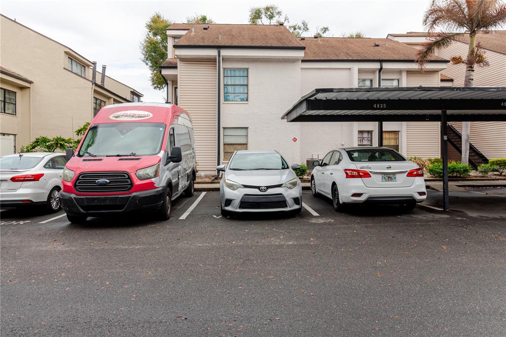 A parking lot with a plumbing van and two cars sits before a multi-story building — 4835 PURITAN CIRCLE UNIT 121, TAMPA, FL
