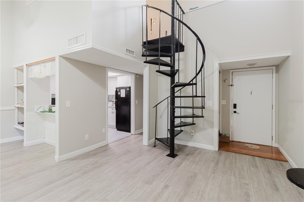 A living area features light wood-look flooring, a black spiral staircase, and an adjacent kitchen — 4835 PURITAN CIRCLE UNIT 121, TAMPA, FL