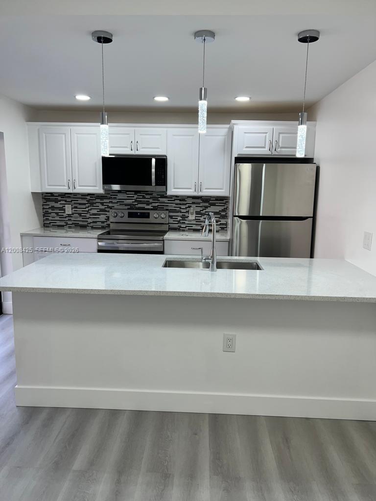 A modern kitchen features white cabinets, stainless steel appliances, and a large quartz-topped island — 736 Mill Valley Pl # 736, West Palm Beach FL 33409, WEST PALM BEACH, FL