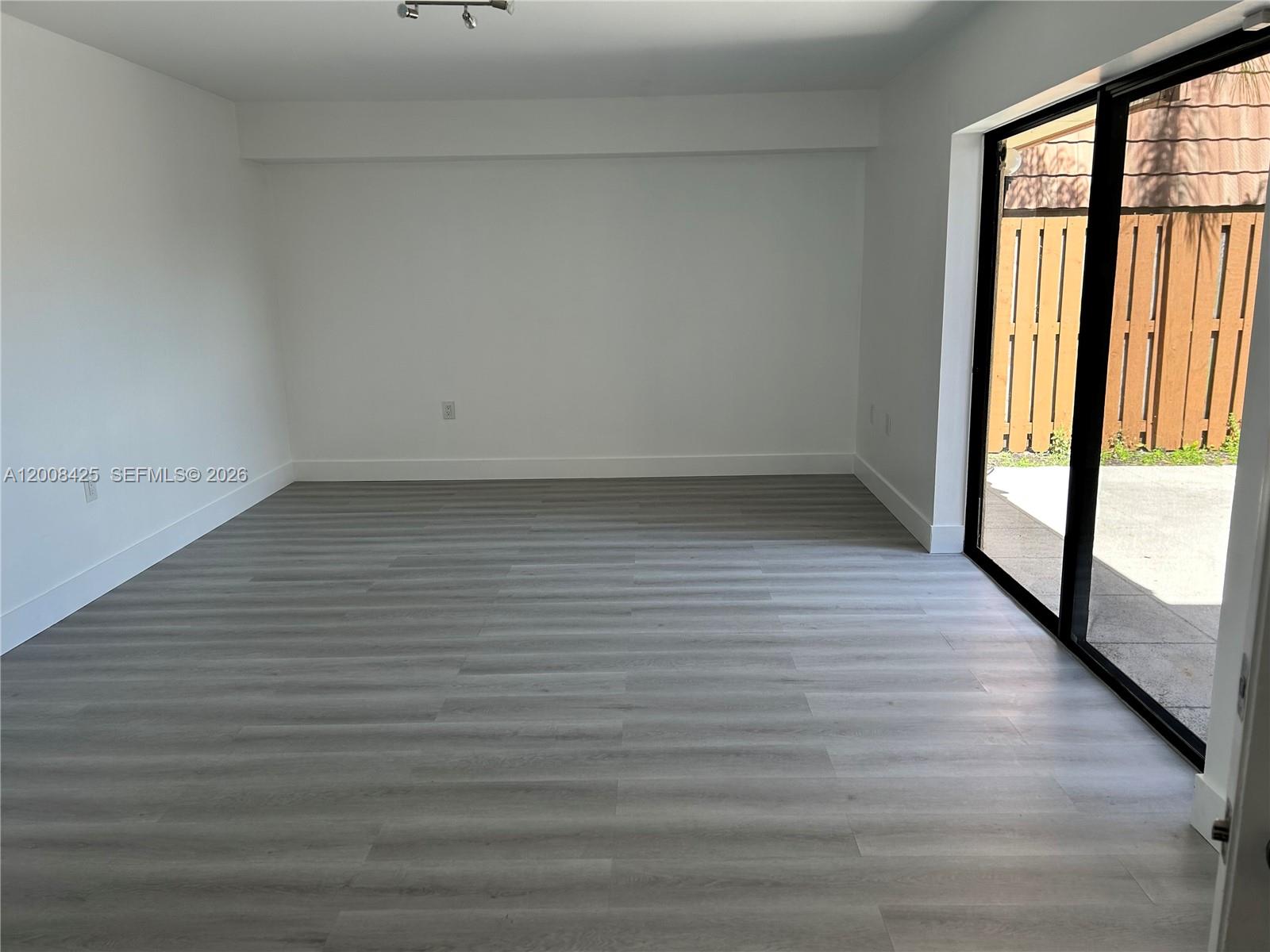 An empty room features light gray wood-look flooring, white walls, and a sliding glass door — 736 Mill Valley Pl # 736, West Palm Beach FL 33409, WEST PALM BEACH, FL