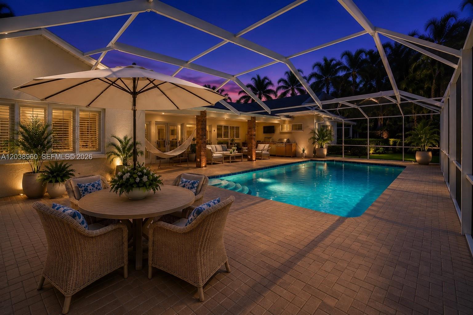 A patio with a dining set and umbrella overlooks a swimming pool at dusk — 13025 SW 108th Ave, Miami FL 33176, MIAMI, FL