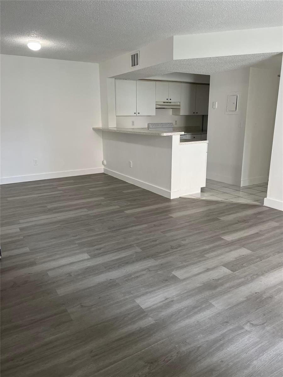 An open-concept living area features gray wood-look flooring and a kitchen with white cabinets — 18860 NW 57th Avenue # 106, Hialeah FL 33015, HIALEAH, FL