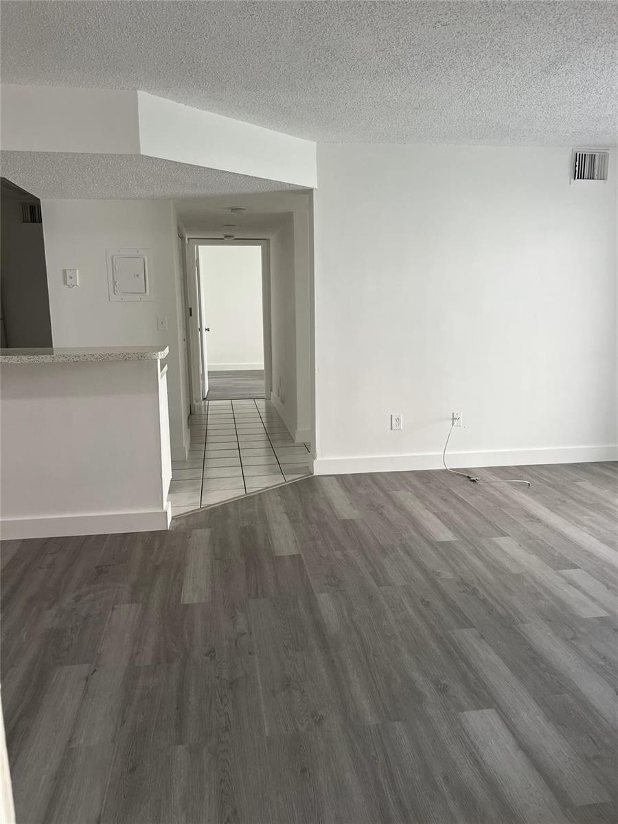 An open living area features gray wood-look flooring, white walls, and a tiled hallway entrance — 18860 NW 57th Avenue # 106, Hialeah FL 33015, HIALEAH, FL