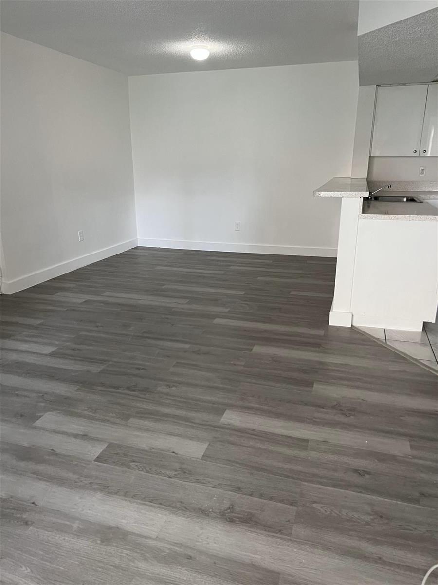 An empty room with grey wood-look flooring and a breakfast bar leading to a kitchen — 18860 NW 57th Avenue # 106, Hialeah FL 33015, HIALEAH, FL