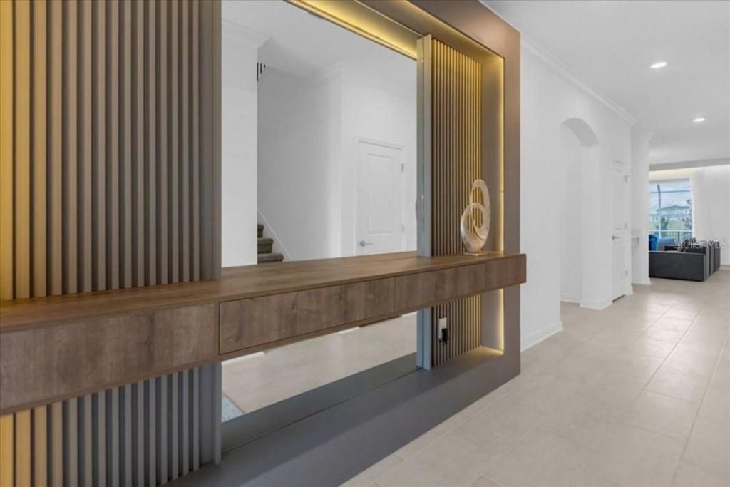 A modern entryway features a wood-paneled floating console table with a large mirror and lighting — 8967 PLAY THROUGH DR, DAVENPORT, FL