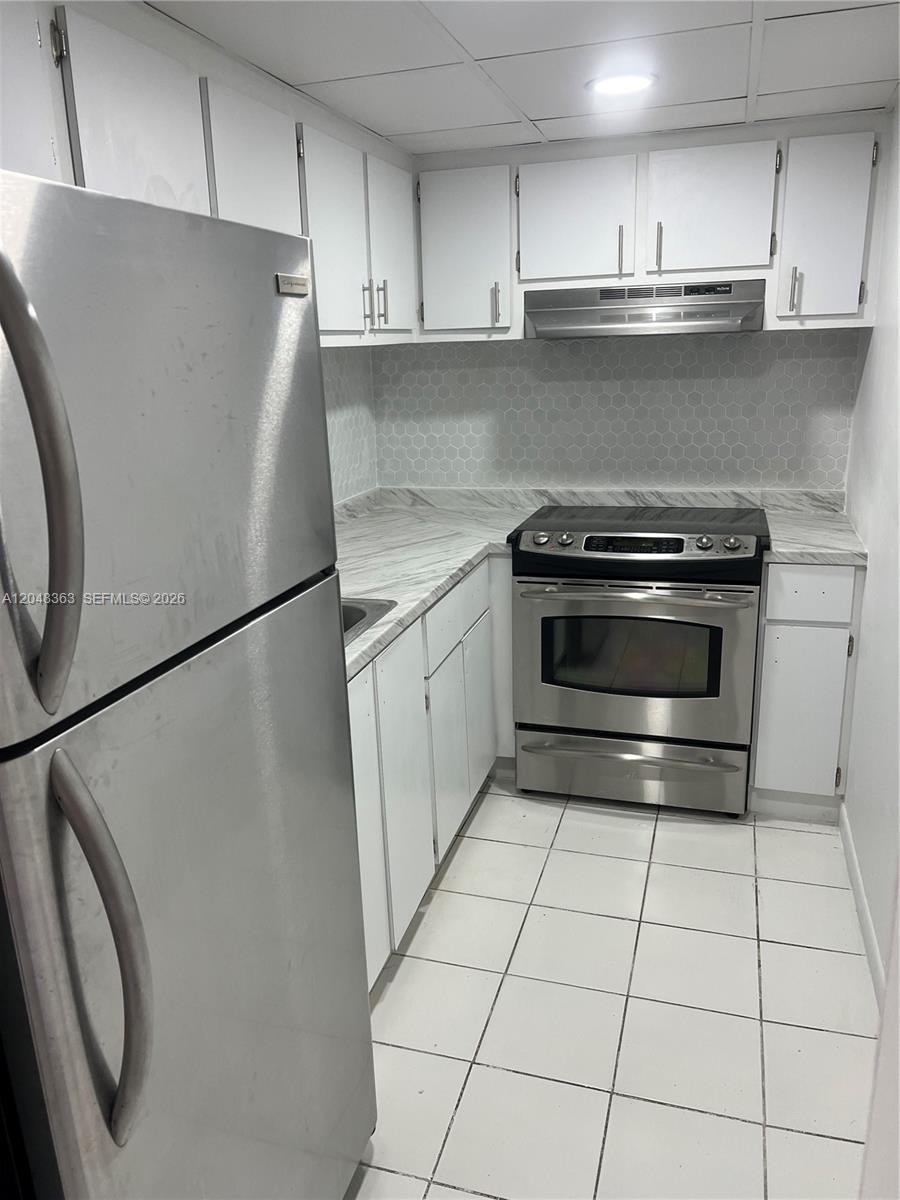 A galley kitchen features white cabinets, stainless steel appliances, and a gray hexagonal tile backsplash — 4715 NW 7th St # 2, Miami FL 33126, MIAMI, FL