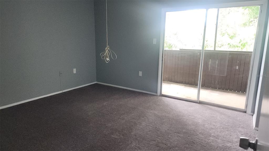 A bedroom with gray walls, dark carpeting, and a sliding glass door leading to a balcony — 1818 WARRINGWOOD DRIVE UNIT GE, ORLANDO, FL