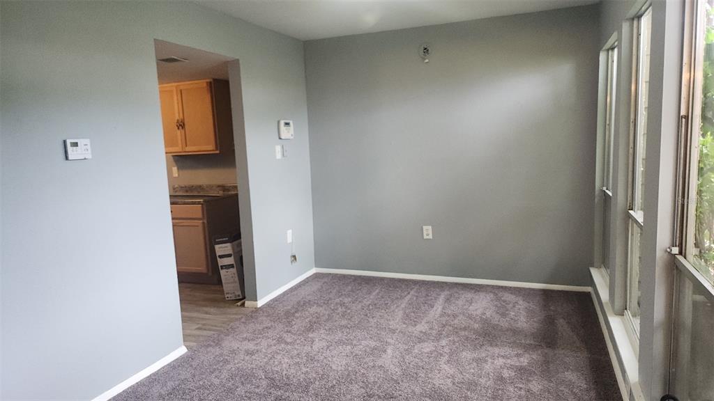 A carpeted room with gray walls and a doorway leading to a kitchen — 1818 WARRINGWOOD DRIVE UNIT GE, ORLANDO, FL
