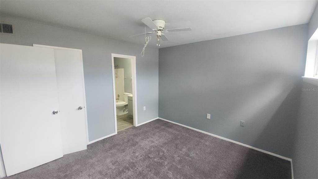 A bedroom with gray walls, gray carpet, a ceiling fan, and an attached bathroom — 1818 WARRINGWOOD DRIVE UNIT GE, ORLANDO, FL