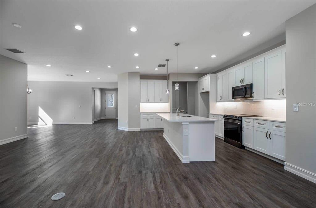 A modern kitchen with white cabinets and a central island opens into a living area — 12418 SW 62ND PLACE, OCALA, FL