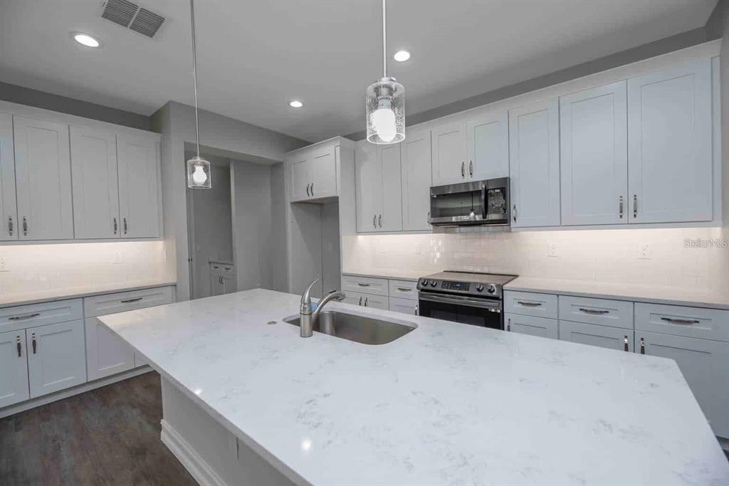 A modern kitchen features light gray cabinets, a white quartz island, and stainless steel appliances — 12418 SW 62ND PLACE, OCALA, FL