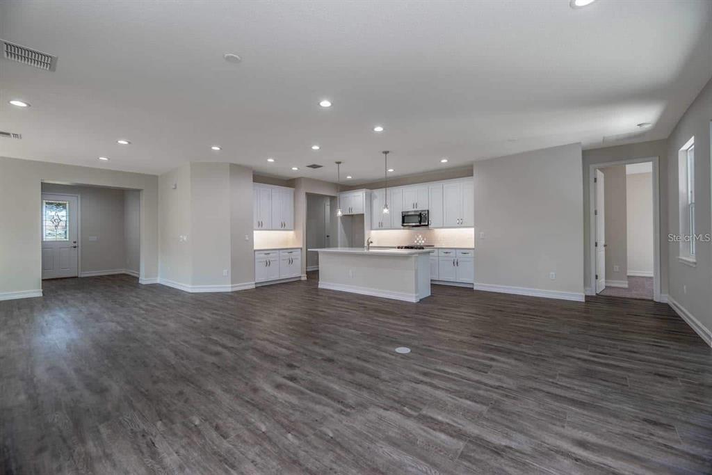 An open-concept kitchen and living area with white cabinets, a central island, and wood-look flooring — 12418 SW 62ND PLACE, OCALA, FL